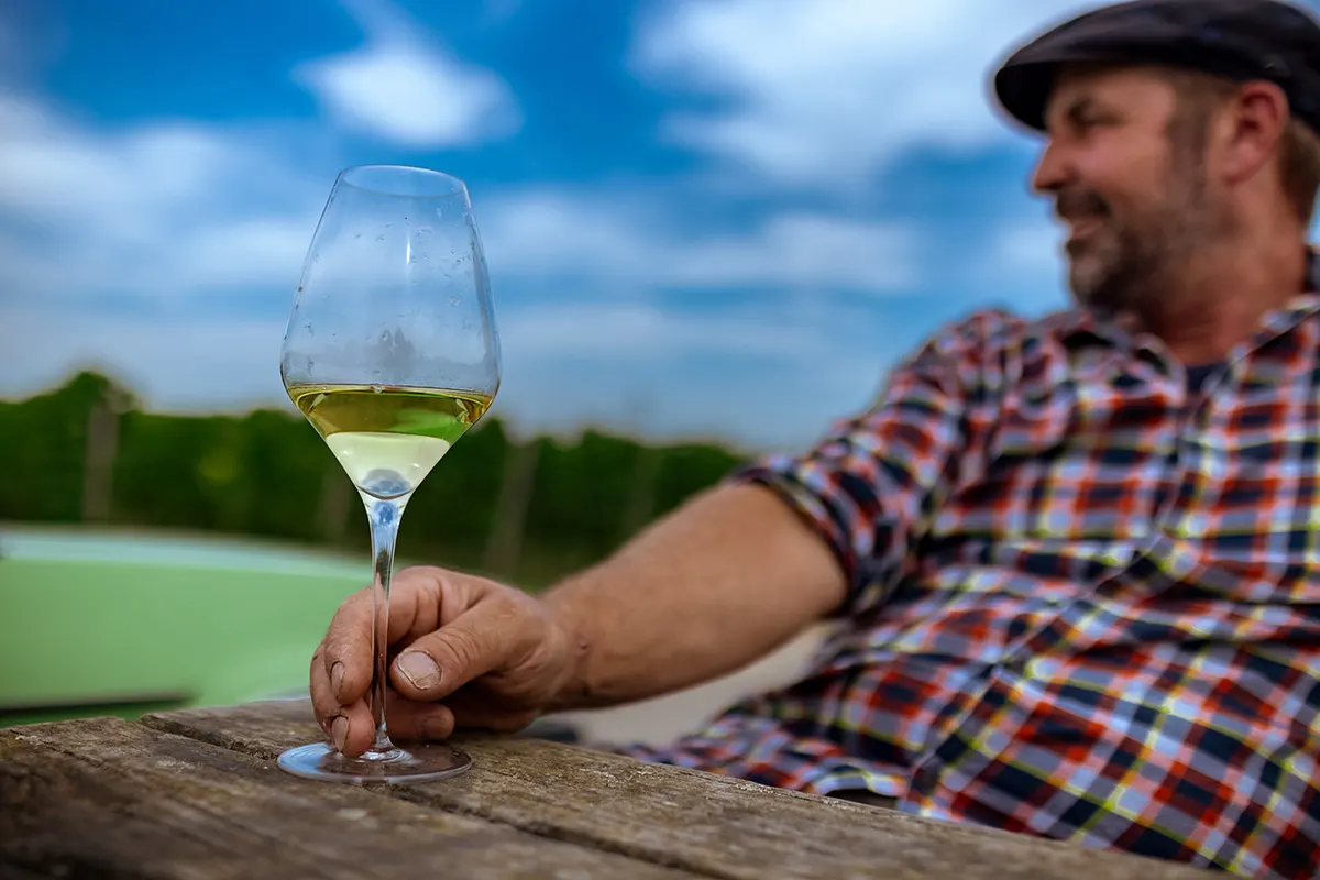Ein Mann sitzt an einem Holztisch mit einem Glas Weißwein
